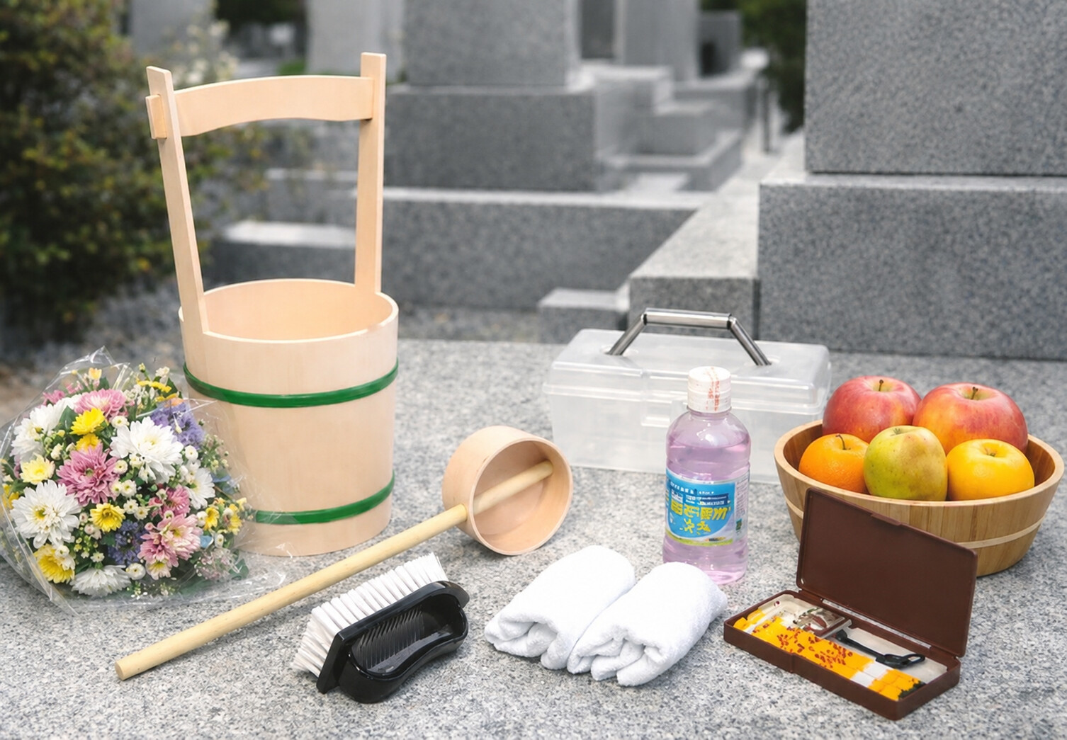 堺市のお墓参りで使用する桶や柄杓、花、お供え物などを並べた供養用品の画像。