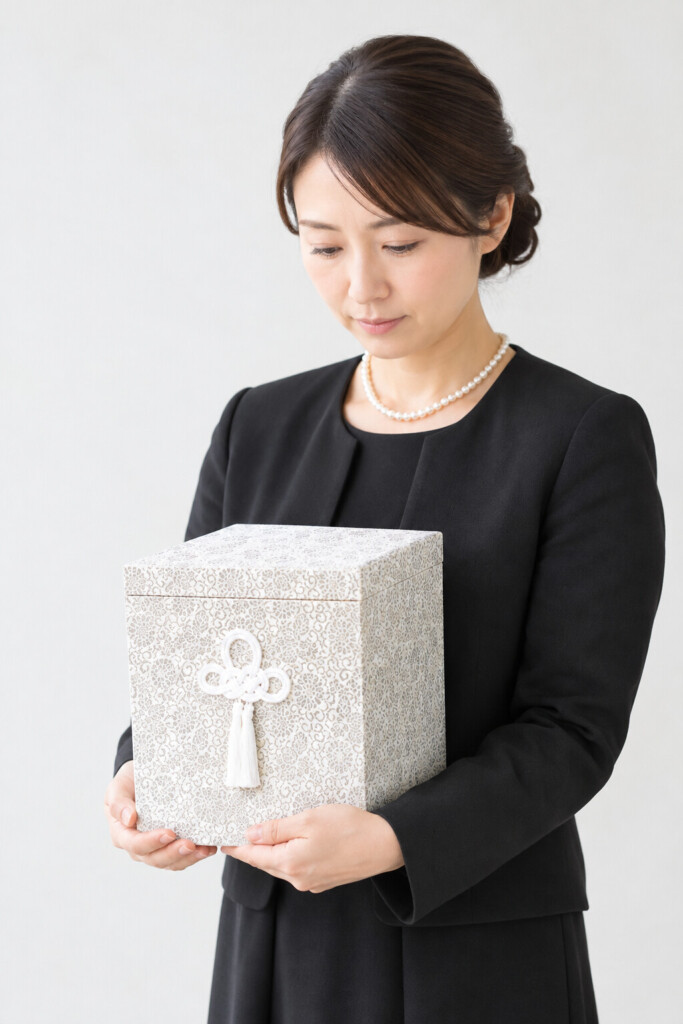 堺市で葬儀を終えた後の収骨について考える方に向けた、白い骨箱を抱える喪服姿の女性のイメージ画像